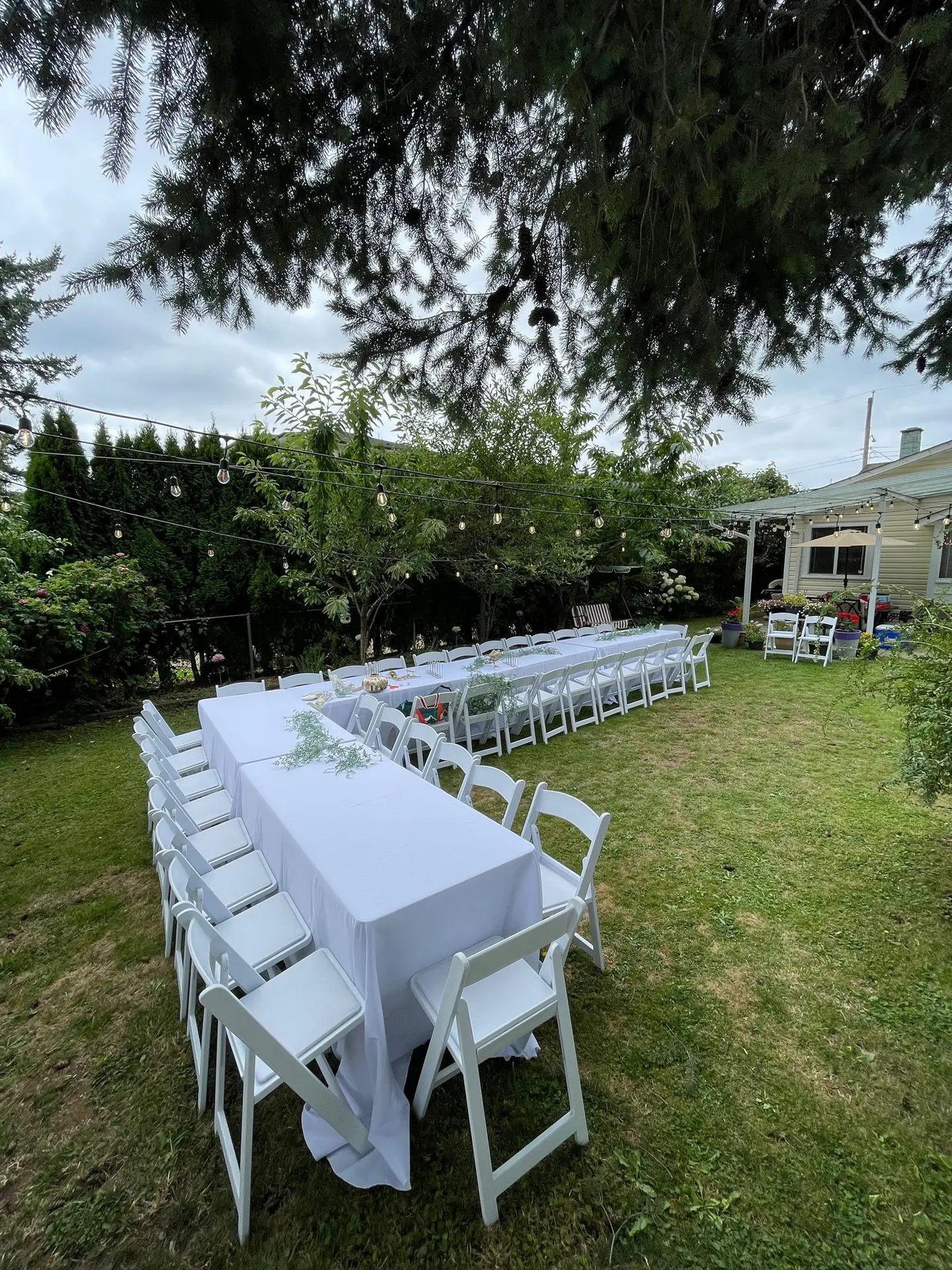Long white-clothed tables and white chairs at a backyard celebration