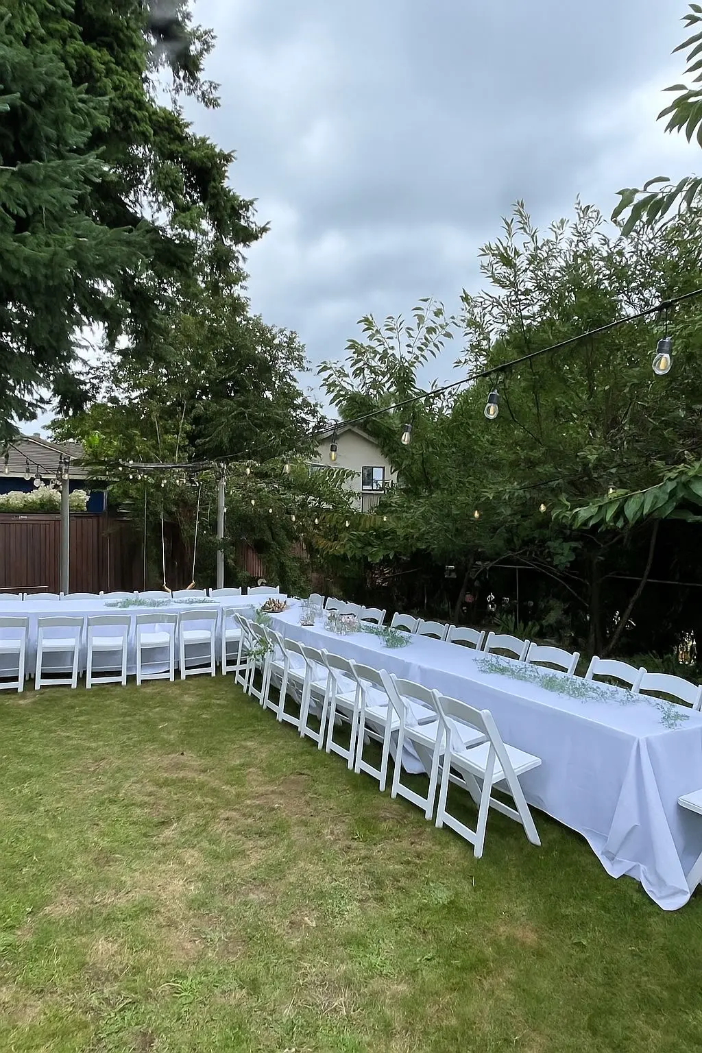 Outdoor dinner tables with white chairs beneath string lights