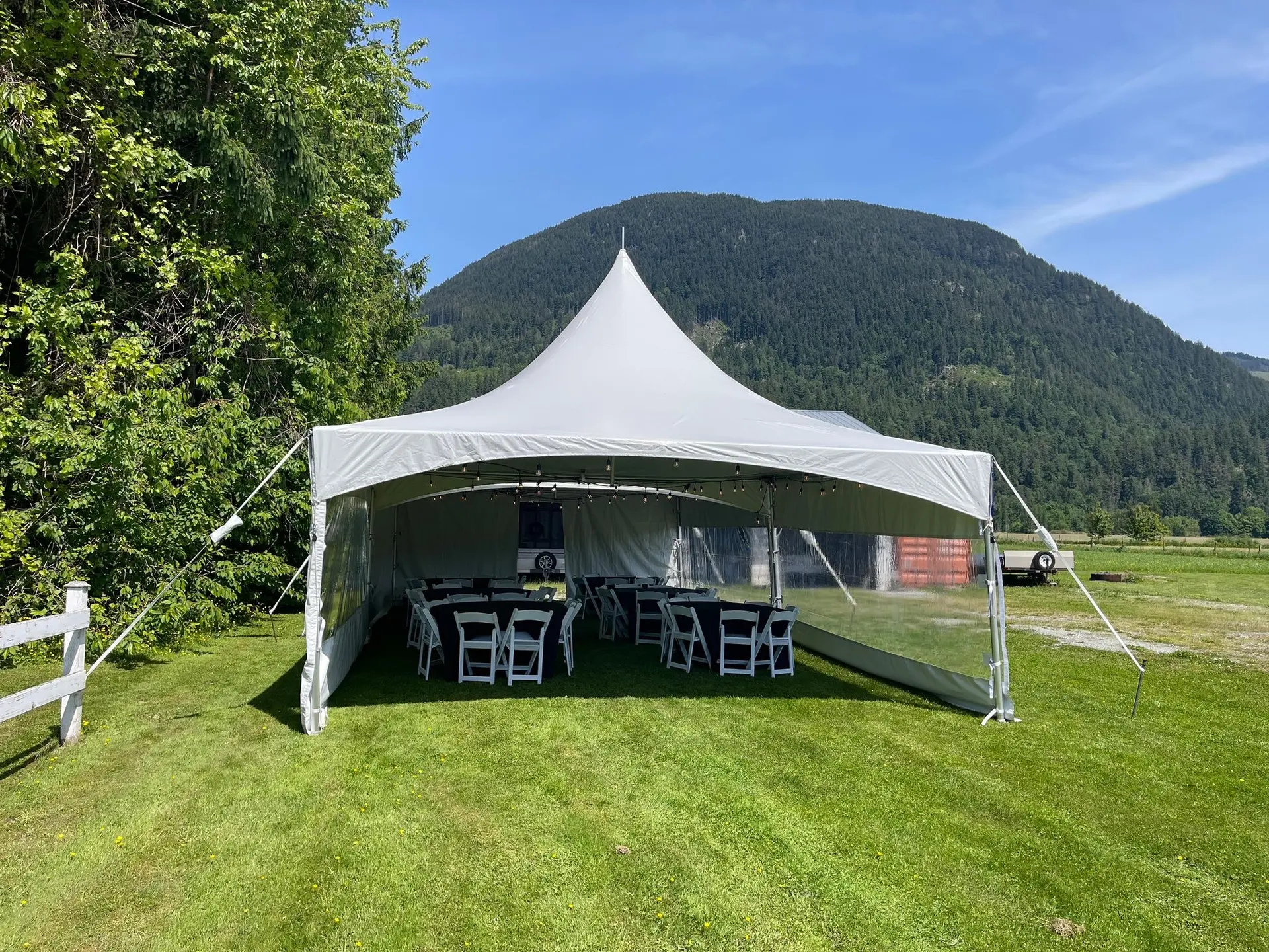 White high-peak event tent with tables and clear side walls near the mountains